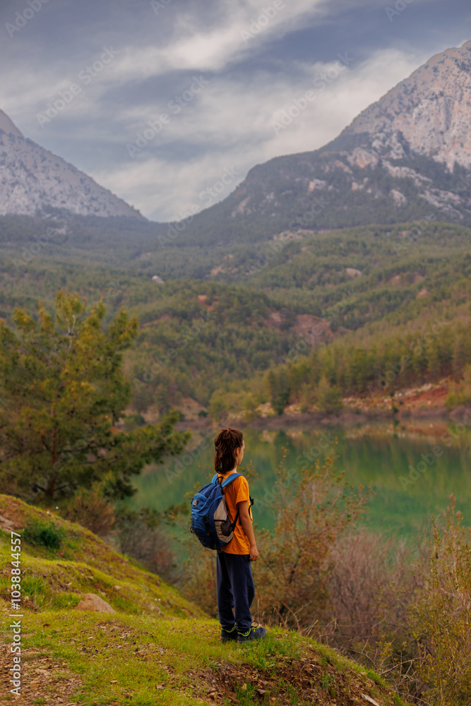 Sticker summer camp. a boy with a backpack looks at a beautiful mountain lake. Relaxed, peaceful, thoughtful, happy and free child on a mountain lake.