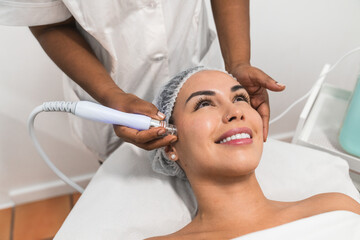 Beautician using modern equipment providing radiofrequency treatment to woman