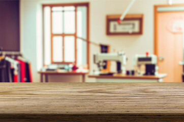 Blur Sunny Fashion Design Studio and wooden table top. We See, Hanging Clothes, Sewing Machine and Various Sewing Related Items on the Table, Mannequins Standing, Colorful Fabrics.