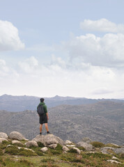 Male person hiking on a mountain trail, standing at the top of the mountain to admire the landscape