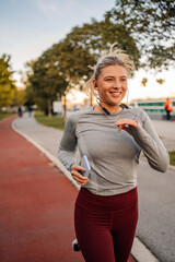 Young sporty woman running in the park listening music and smiling