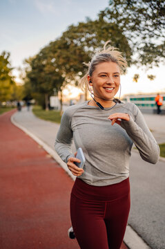 Young sporty woman running in the park listening music and smiling