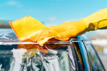 Vibrant yellow cloth polishing the roof of a car under a bright blue sky during a sunny day
