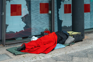A quiet moment of rest for a person on the streets wrapped in a red blanket near modern...