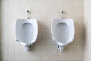 Frontal detail of the interior of a public bathroom with two urinals for men. The decoration is clean and pleasant. Light tiles. Concept of cleanliness and choice, left or right