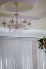 A chandelier with six lights hanging from it. The lights are lit up and the chandelier is white