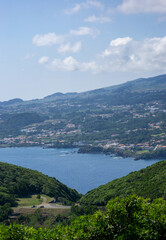 Obraz premium Aerial view of a coastal Portugese town on a hilly island with lush greenery and the Atlantic Ocean in the background. Scattered houses and winding roads are visible in the scenic landscape.