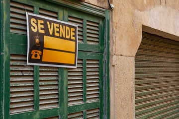 Obraz premium Door of a house with a green Mallorcan shutter in a state of abandonment, with a for sale sign written in Spanish. Image of the problem of access to housing for the population in Spain