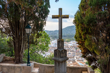 Sculpture of a stone cross in the Calvary of the Majorcan town of Arta, with the town in the background at sunrise. Spain