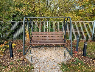 A vibrant red and white stop barrier is positioned on a paved path, surrounded by fallen leaves, signaling pedestrians to halt and ensure safety as they navigate the walkway.