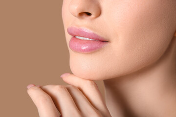 Beautiful young woman touching chin on brown background, closeup