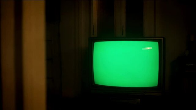 tv with a green screen on the screen, dimli lit room