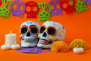 Painted skulls and glowing candles on orange background. Celebration of Mexico's Day of the Dead...
