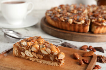 Wooden boards of cut sweet tart with different nuts on white background