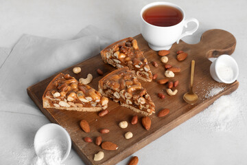 Wooden board of cut sweet tart with different nuts and cup of tea on white background