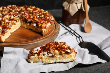 Wooden board of cut sweet tart with different nuts and caramel on black background