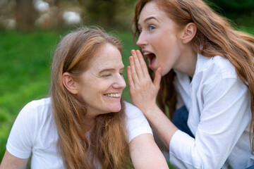 Friends share a joyful secret while enjoying a sunny afternoon in a lush green park