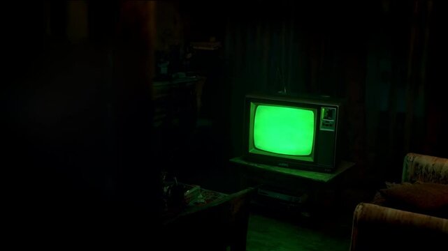 tv with a green screen on the screen, dimli lit room