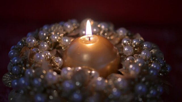 Candela natalizia colore oro accesa e posata al centro di una ghirlanda di perle e petali finti