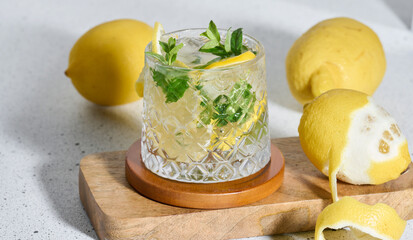 Transparent glass with lemon slices, mint leaves and ice cubes on white table