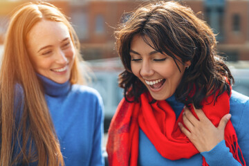 Obraz premium Joyful friendship between two women with bright scarves enjoying their day in a bustling city at sunset