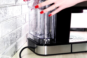 Girl puts water container in coffee machine. Water boiler. Close-up. Making coffee at home
