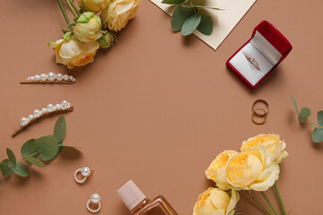 Frame made of wedding rings, flowers and bride's accessories on brown background
