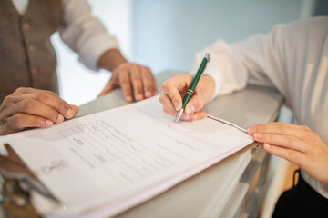 A person is signing a document with a green pen. The person's hand is holding the pen and their...