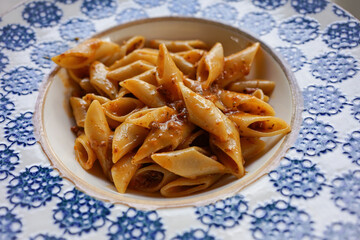 Close-up of penne pasta bolognese served in a white and blue ceramic bowl with rich, meaty sauce. This image is perfect for illustrating delicious Italian cuisine, comfort food, or food presentation.