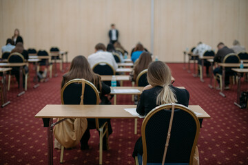 A lesson, an exam, a lecture in a large audience. The view from the back.  A group of students are sitting at their desks, writing a lecture or doing an assignment