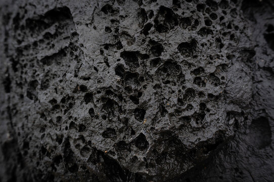 Black background grey lava stone with erosion holes caused by wind, water and weather. Backdrop surface weathered, porous and furrowed. Rare earths.
