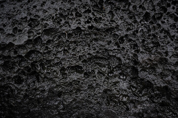 Black grey background lava stone with erosion holes caused by wind, water and weather. Backdrop surface weathered grunge and furrowed.
