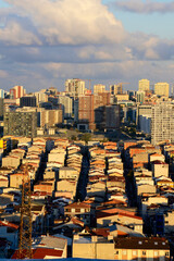 Fototapeta premium Aerial view of densely packed residential rooftops in Istanbul with modern high-rise buildings and a cloudy sky in the background. 