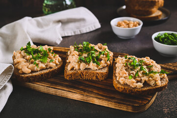 Appetizing sandwiches on grain bread with mashed beans and greens on a board on a table