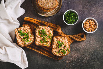 Appetizing sandwiches on grain bread with mashed beans and greens on a board top view