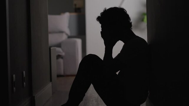 Depressed young man sitting on floor. Portrait of anxious handsome man on the floor having business or personal problems feeling stressed and desperate
