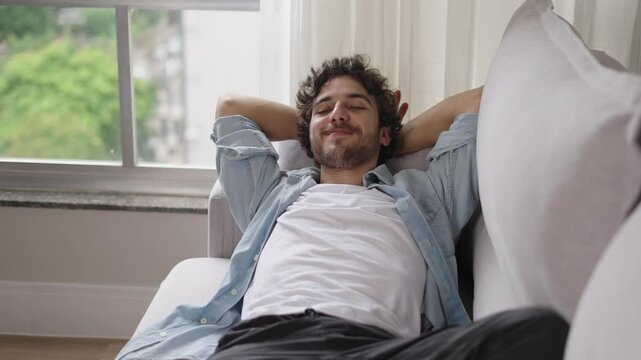 Happy lazy young man relax daydream meditate sit on comfortable sofa at home in living room, calm guy rest breathing fresh air having nap with eyes closed feel peace of mind, no stress free relief
