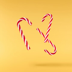 Obraz premium Christmas holliday image, Christmas bauble in shape of a christmas stick lolipop falling in the air isolated on yellow background