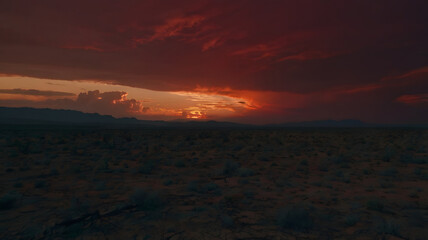 Fototapeta premium Dark red sunset sky over the expansive desert, with clouds and a fiery orange-red sun, evoking an Oriental evening, perfect for a dramatic nature backdrop