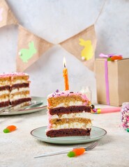 Sliced ​​Birthday cake with pink cream, carrot and beetroot layers and burning candle on green ceramic plate on light concrete background. Happy Birthday concept.
