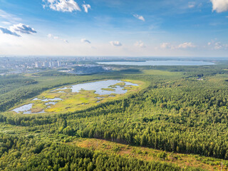 Big lake with green shores in bright sun light and city on horizon, aerial landscape. Recreation concept. Aerial view