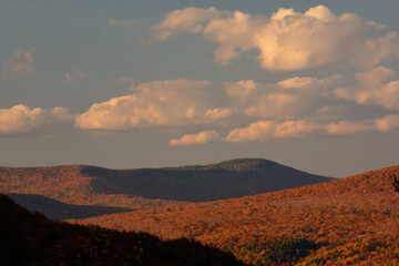 Late autumn afternoon scene in White Mountains of New Hampshire. Colorful fall foliage, long shadows, and sunlit clouds over mountain tops.