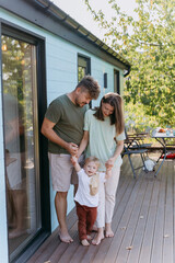 Happy family moment with parents helping their toddler walk on deck, enjoying a peaceful outdoor day