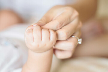 A close-up of an adult hand gently holding a baby's hand, symbolizing care, tenderness, and the...