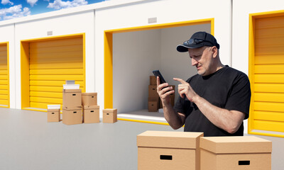 Man near storage unit. Guy is tenant of self warehouse garage. Owner of pantry uses telephone. Rent outdoor storage unit via smartphone. Man smiling standing in front of storage boxes