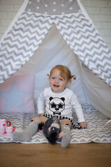 Adorable beautiful happy smiling ginger-haired toddler little girl is playing with her toys sitting in a teepee wigwam © Tina