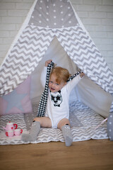 Adorable beautiful happy smiling ginger-haired toddler little girl is playing with her toys sitting in a teepee wigwam © Tina
