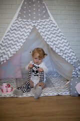 Adorable beautiful happy smiling ginger-haired toddler little girl is playing with her toys sitting in a teepee wigwam © Tina