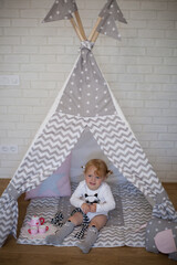 Adorable beautiful happy smiling ginger-haired toddler little girl is playing with her toys sitting in a teepee wigwam © Tina