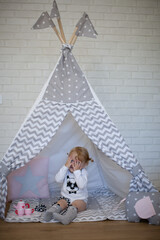 Adorable beautiful happy smiling ginger-haired toddler little girl is playing peekaboo sitting in a teepee wigwam © Tina